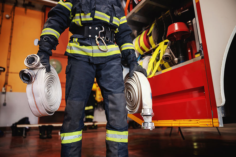Firefighter in protective uniform standing with flattened hose in front of firetruck