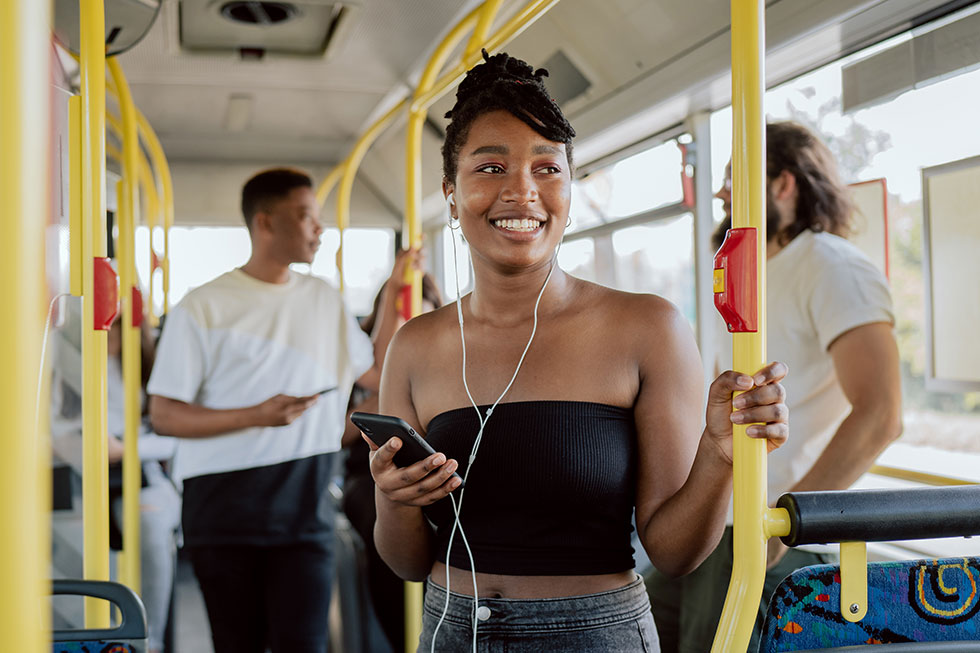 Woman with headphones smiling and standing in a bus with other passengers